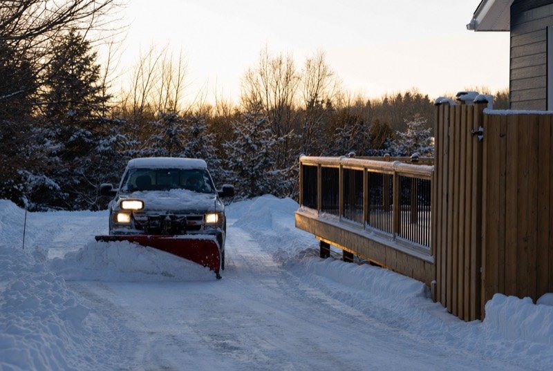 A pickup truck with a plow clearing a country driveway beside a new deck