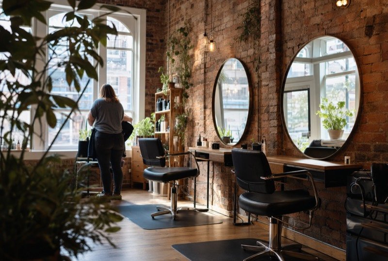 A bright hair salon with exposed red-brick walls and round mirrors